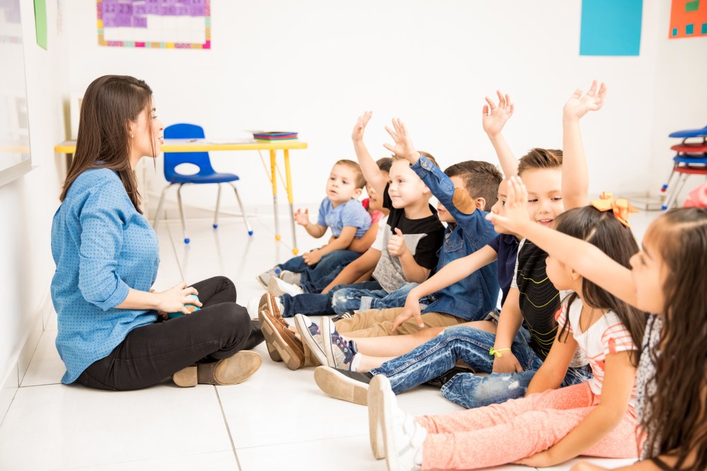 a group of preschool students raising their hands and trying to participate at school